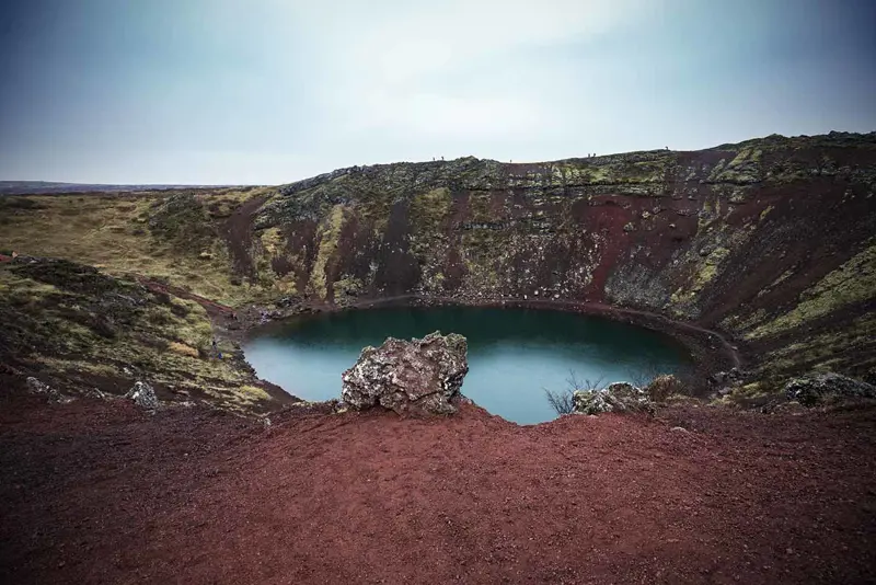 The vibrant red volcanic rock surrounding Kerid Crater Lake, Iceland.
