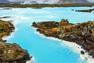 The Blue Lagoon surrounded by lava fields in Iceland with steam rising from the waters in the distance.