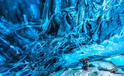Adventurer exploring a striking blue ice cave in Iceland with reflective icy walls, showcasing a must-visit destination on a Travel Reykjavik tour.