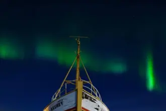 Northern Lights In Hofn Iceland Over Boat In Harbor.