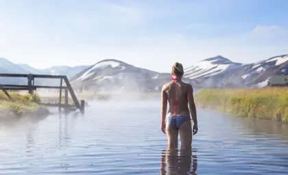 A person soaking in the natural hot springs at Landmannalaugar, surrounded by steam and snowy peaks.