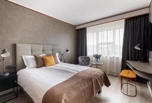 Comfortable double room with a neutral color palette, cozy bed with accent pillows, natural light from a large window, and modern furnishings.