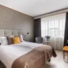 Comfortable double room with a neutral color palette, cozy bed with accent pillows, natural light from a large window, and modern furnishings.