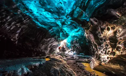 Solo hiker in red standing in an illuminated ice cave under Vatnajökull glacier in Iceland, surrounded by vivid icy walls.