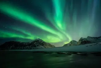 Northern Lights sky reflecting on ice with a mountain backdrop in Iceland.