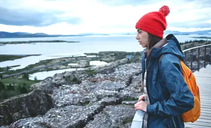 A woman in a red hat and blue jacket gazes over the tectonic rift and lake at Thingvellir National Park in Iceland, a UNESCO World Heritage Site.