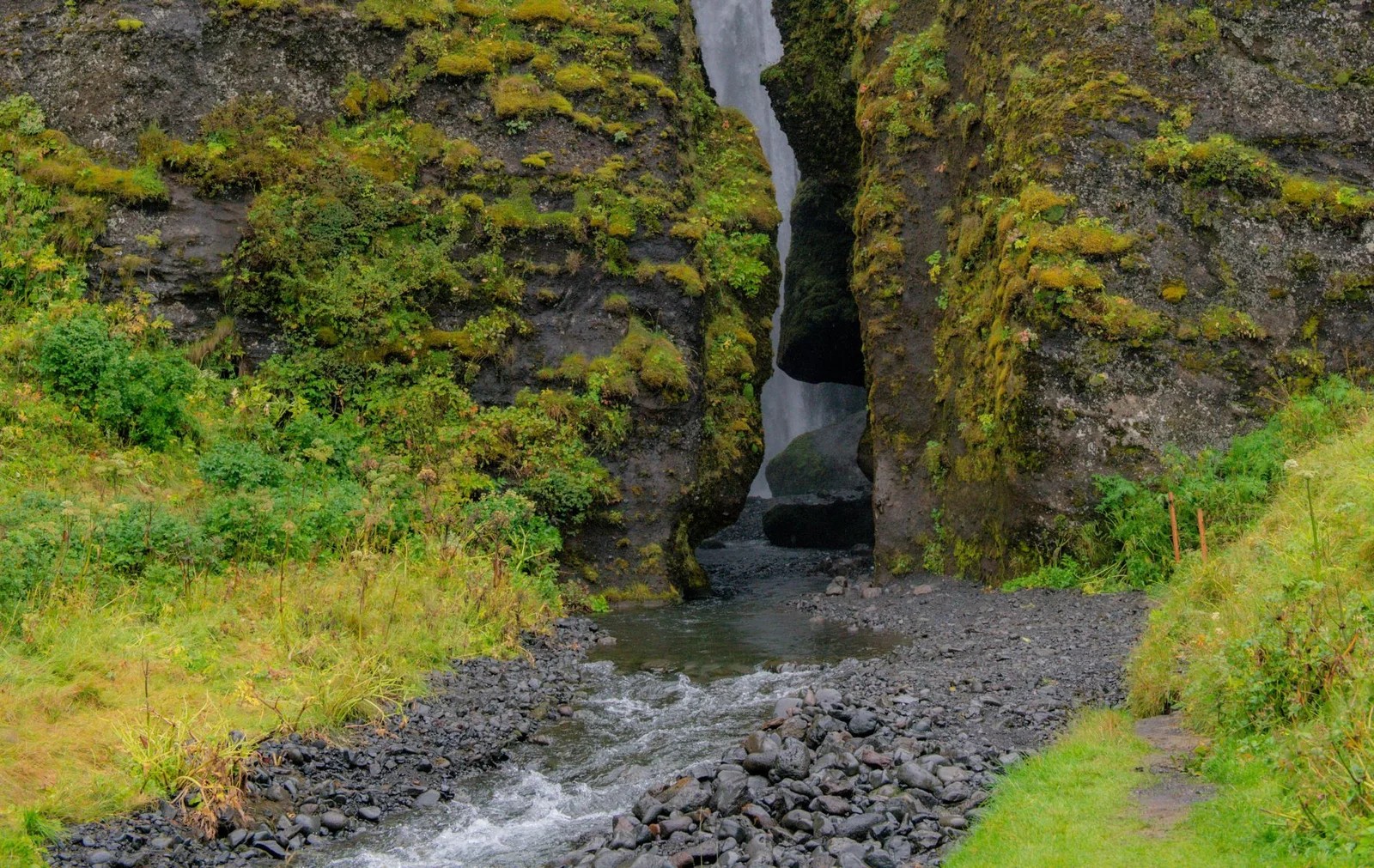 Gljúfrabúi Waterfall partially visible through a narrow rock crevice, with a stream flowing from the gorge entrance.