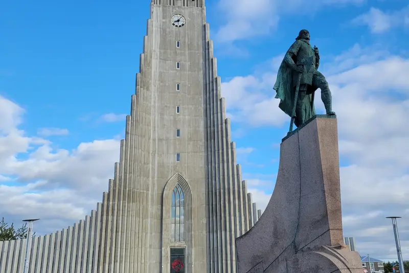 Statue of Leif Erikson in front of Hallgrímskirkja church under a bright blue sky in Reykjavík, Iceland, a popular attraction on city tours.