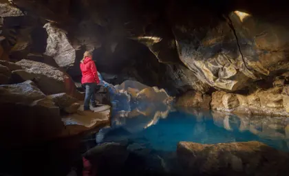 A traveler in a red jacket explores the mystical Grjótagjá cave, known for its geothermal hot spring and dramatic rock formations in Iceland.