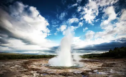 The powerful eruption of Strokkur Geyser in Iceland shooting water into the sky against a backdrop of dramatic clouds.