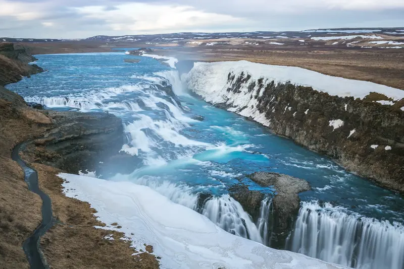 Stunning winter view of Gullfoss Waterfall with icy blue waters cascading down snowy cliffs along the Golden Circle in Iceland
