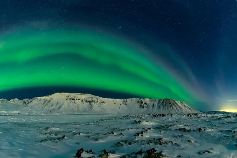 Green northern lights over snowy mountains in winter on northern lights tour with Travel Reykjavík.