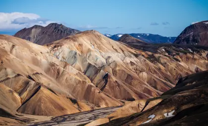 Panoramic view of the striking rhyolite mountains at Landmannalaugar, with layered colors and dramatic ridges under a blue sky, a famed Icelandic highland destination.