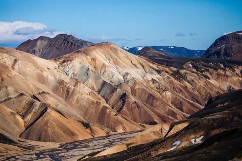 Panoramic view of the striking rhyolite mountains at Landmannalaugar, with layered colors and dramatic ridges under a blue sky, a famed Icelandic highland destination.