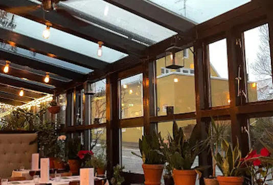 Cozy interior of Snaps Bistro in Reykjavík, featuring glass walls, vibrant plants, and warmly lit dining tables, offering a charming dining atmosphere.