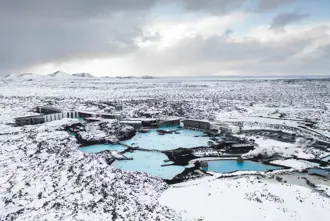 Aerial view of the Blue Lagoon in Iceland during winter, surrounded by snowy lava fields, with geothermal pools and spa facilities nestled in a serene, icy landscape.