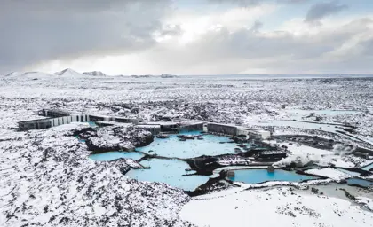 Aerial view of the Blue Lagoon in Iceland during winter, surrounded by snowy lava fields, with geothermal pools and spa facilities nestled in a serene, icy landscape.