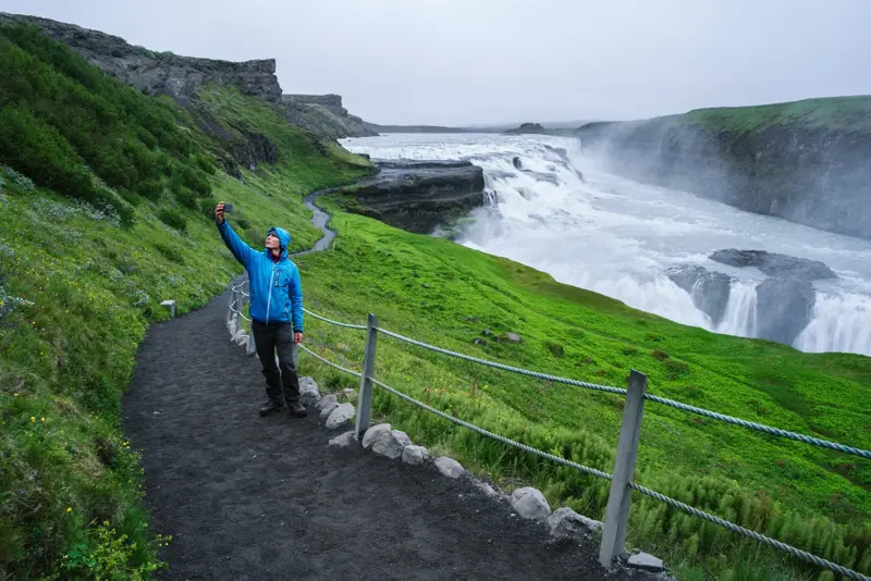 Man taking a selfie with the dramatic Gullfoss waterfall in the background, showcasing the natural beauty of Iceland’s Golden Circle.