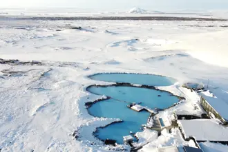 Aerial view of Mývatn nature baths in winter and geothermal pool surrounded by snowy landscapes in Iceland, with bright blue waters contrasting against the white winter terrain.