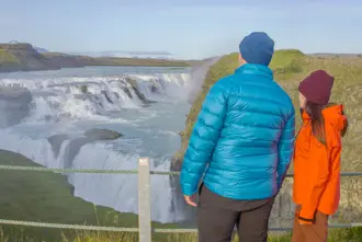 Two people view Gullfoss from the waterfall's lookout point.
