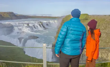 Two people view Gullfoss from the waterfall's lookout point.