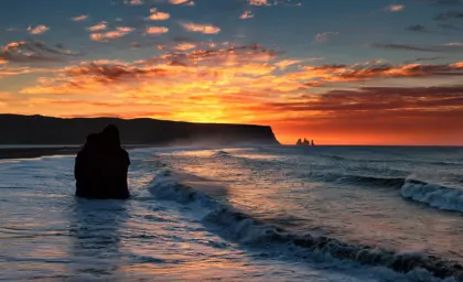 Reynisfjara at sunset on South Coast Day Tour from Reykjavík, seen with Reynisdrangar sea stacks at the horizon.