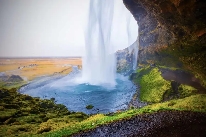 Seljalandsfoss waterfall in Iceland, cascading down a cliff with a walkway that allows visitors to walk behind the falls.