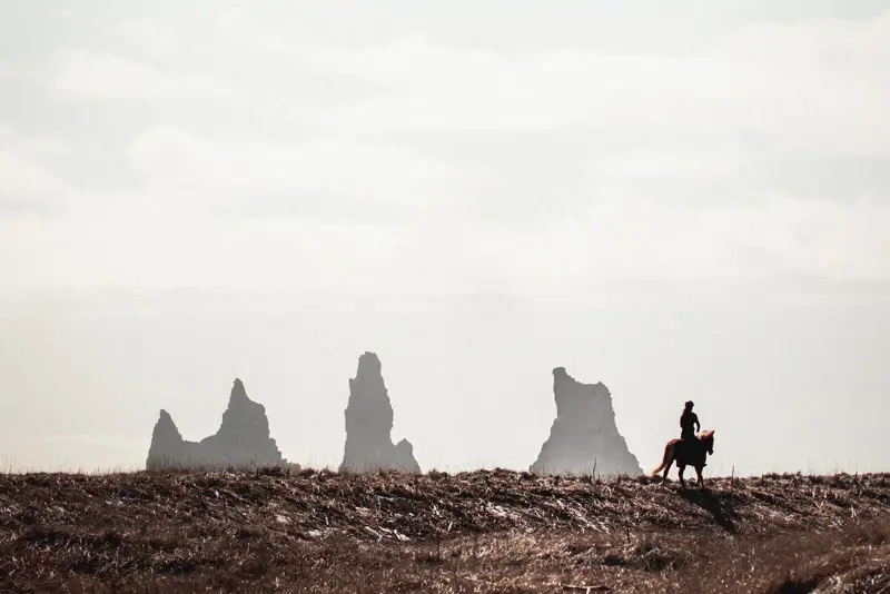 Reynisdrangar in the distance behind a person riding a horse on the horizon.