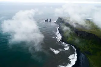 Aerial view of Reynisdrangar rock formations on the black sand coast, shrouded in mist and surrounded by dramatic cliffs in South Iceland.