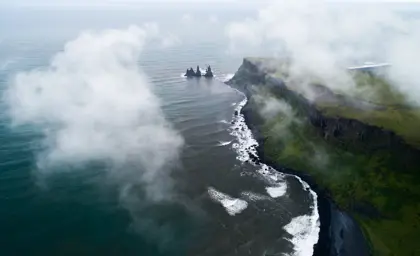 Aerial view of Reynisdrangar rock formations on the black sand coast, shrouded in mist and surrounded by dramatic cliffs in South Iceland.