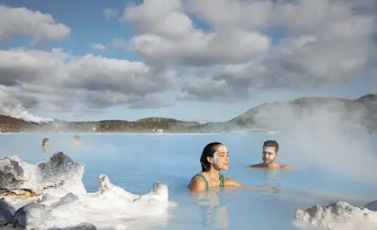 Blue Lagoon guests swimming in the blue water with steam rising to the blue sky. 