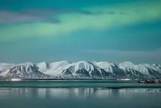 Fade Northern Lights over Akureyri and snowy mountains in Iceland.