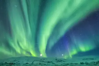 Green And Blue Northern Lights Over Snowy Mountains Iceland.