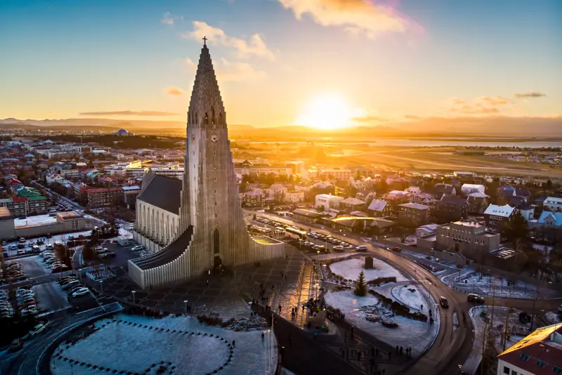 A stunning aerial view of Hallgrímskirkja at sunrise in Reykjavík, Iceland, with golden light illuminating the iconic church and cityscape. Reykjavík city tour by Travel Reykjavík.