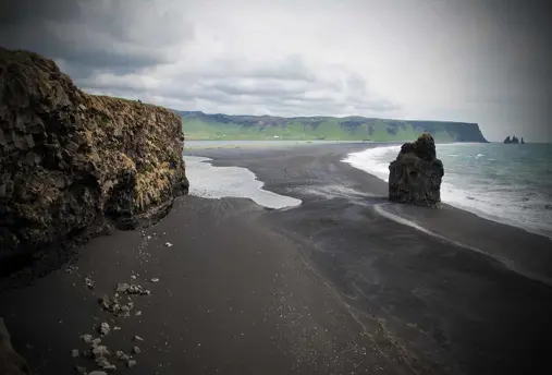 A view of Reynisfjara black sand beach with rugged cliffs and ocean waves in South Iceland.
