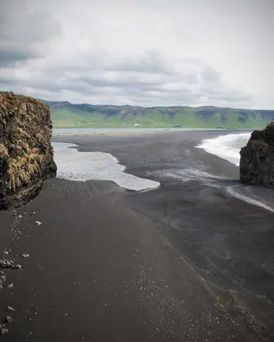 A view of Reynisfjara black sand beach with rugged cliffs and ocean waves in South Iceland.