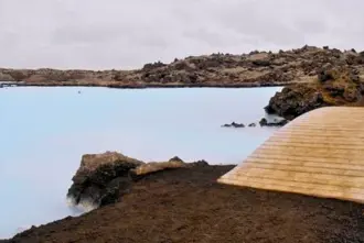 Wooden footbridge over milky water of the Blue Lagoon on a cloudy day in Iceland.