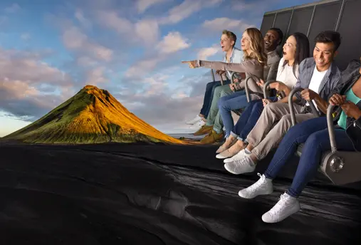 Enthusiastic group on FlyOver Iceland ride, suspended over a scenic Icelandic mountain landscape.
