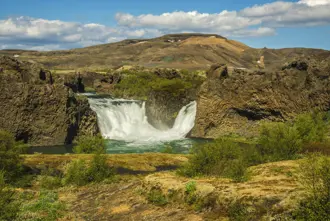Þjórsárdalur valley with views of Hjálparfoss waterfall surrounded by moss covered ground and lava cliffs.