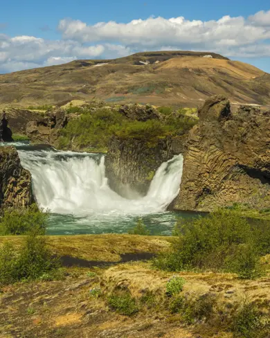 Þjórsárdalur valley with views of Hjálparfoss waterfall surrounded by moss covered ground and lava cliffs.