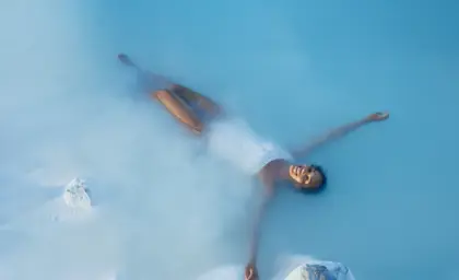 Woman peacefully floating in the Blue Lagoon’s milky blue waters in Iceland, enjoying a serene spa experience surrounded by natural volcanic rocks.