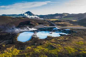Aerial view of Mývatn Nature Baths and Geothermal Spa pools amid Iceland’s rugged volcanic landscape, with steam rising against the scenic mountain backdrop.
