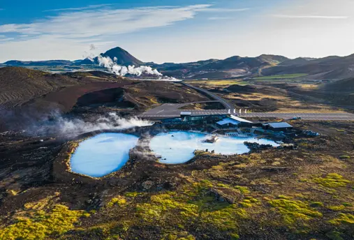 Aerial view of Mývatn Nature Baths and Geothermal Spa pools amid Iceland’s rugged volcanic landscape, with steam rising against the scenic mountain backdrop.