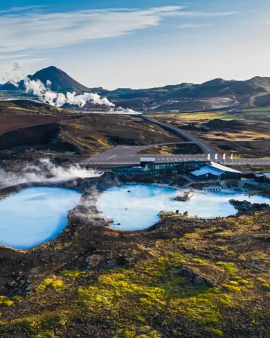 Aerial view of Mývatn Nature Baths and Geothermal Spa pools amid Iceland’s rugged volcanic landscape, with steam rising against the scenic mountain backdrop.