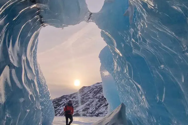Traveler exploring a beautiful glacier ice cave with icy blue walls during a South Shore Blue Ice Cave Tour in Iceland.