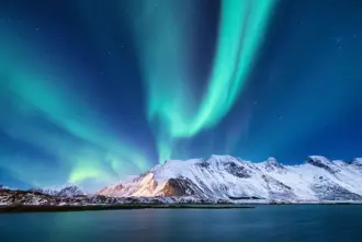 Northern Lights above snowy mountains next to ocean in winter in Iceland.