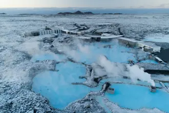Aerial view of the Blue Lagoon geothermal spa in Iceland during winter, showcasing its steaming blue waters surrounded by a snow-covered volcanic landscape.