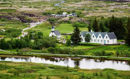 Scenic view of Þingvellir National Park showcasing lush greenery, a historic church, and visitors exploring the landscape, highlighting the natural beauty and cultural significance of Iceland's UNESCO World Heritage Site.