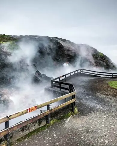 Deildartunguhver geothermal hot spring with steam rising above the fence and mossy ground.