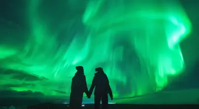 Couple holding hands under dazzling green northern lights in Iceland, reflecting in a still icy lagoon for a magical winter experience.